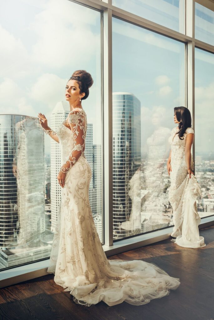 Two brides in wedding gowns by floor-to-ceiling windows overlooking the Houston skyline